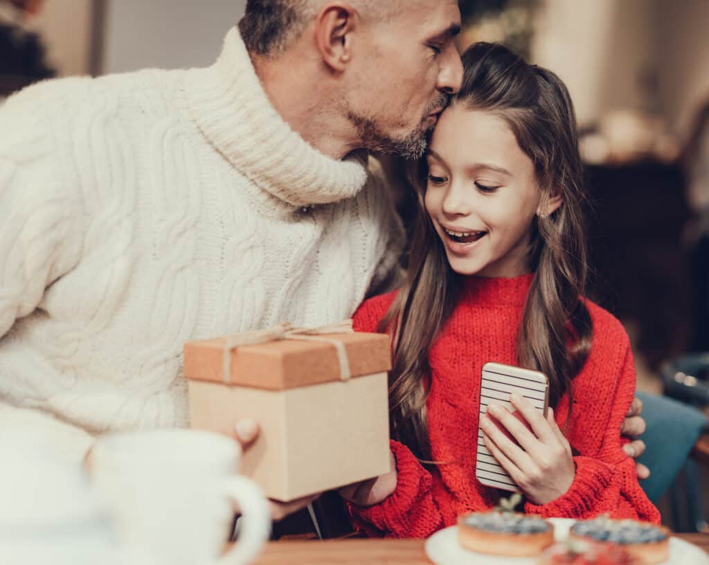 Man kissing forehead of young girl receiving a wrapped gift