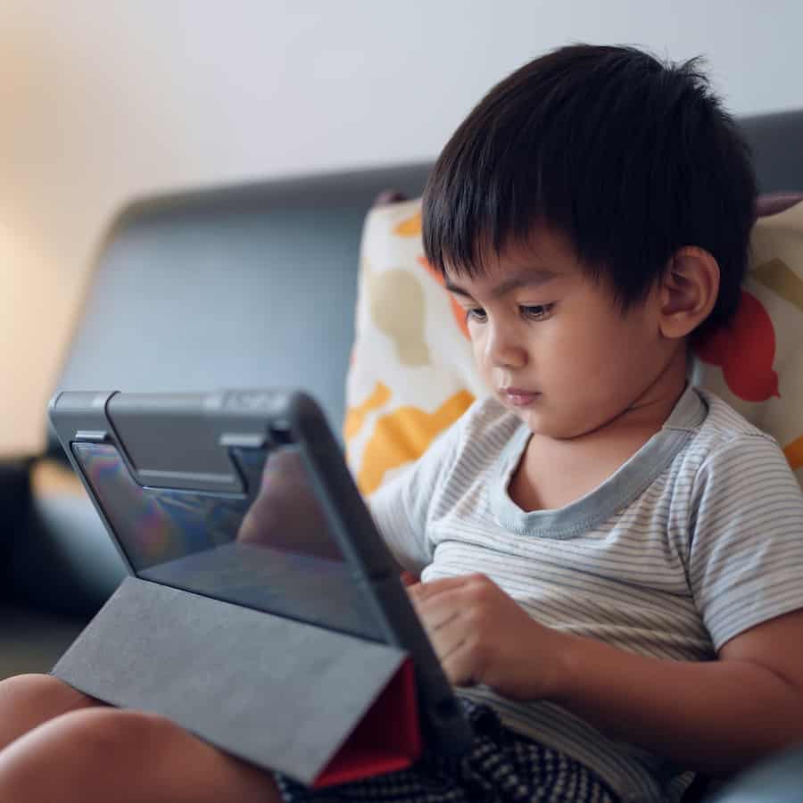 A young boy uses an iPad on the couch