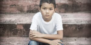A tender age Asian boy sits alone on steps looking at the camera