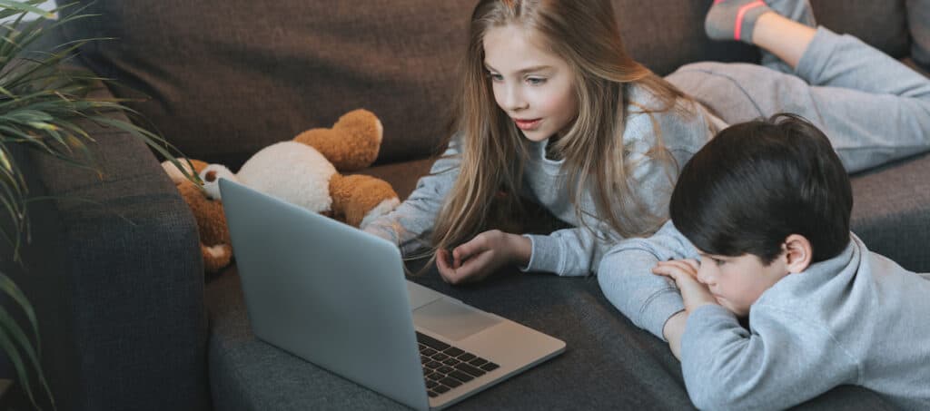 A young brother and sister use a MacBook on a couch in their living room