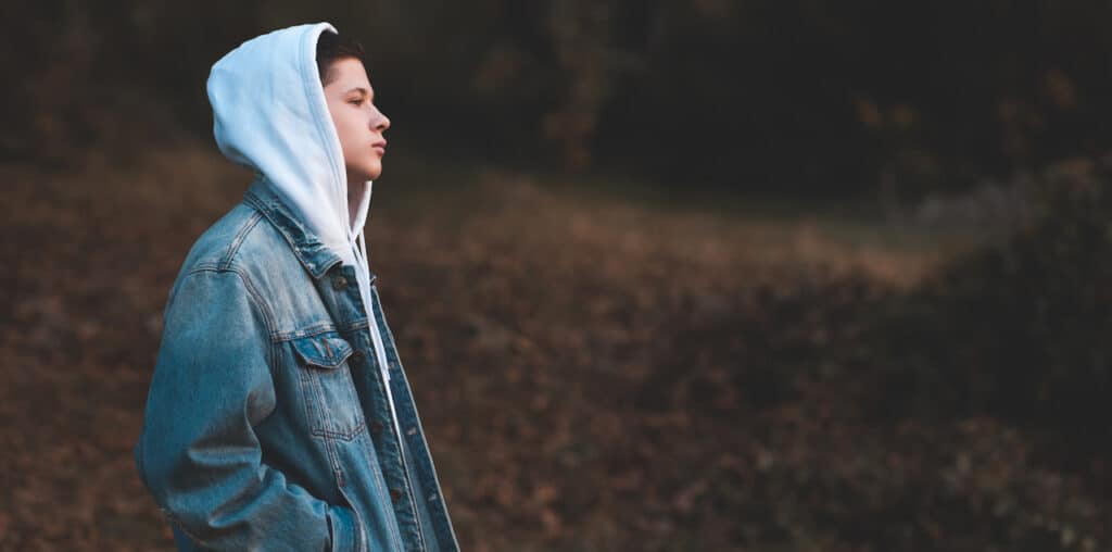 15-16 year old teen boy wearing denim jacket and white hoodie standing outdoors in the leaves.